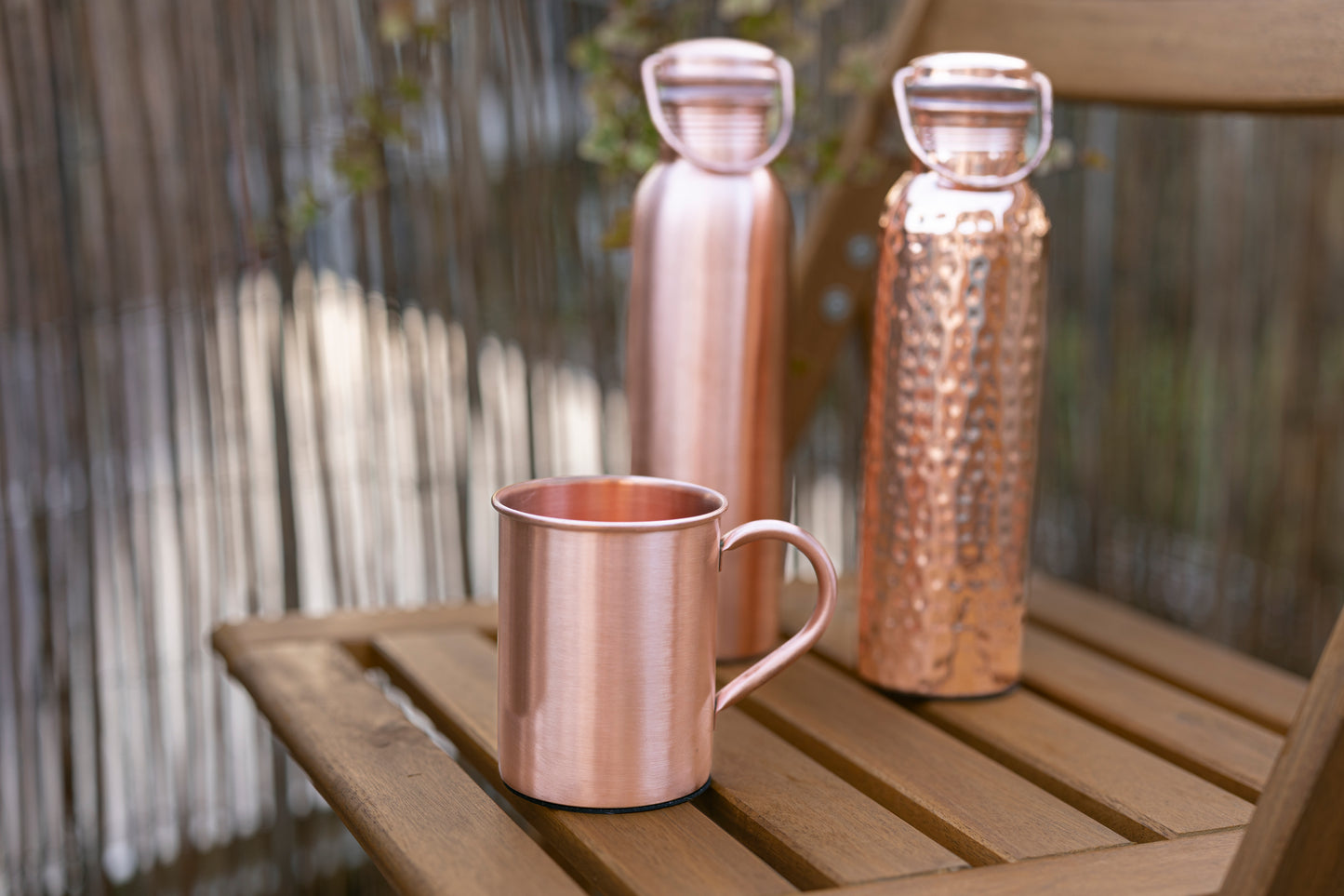 Botellas de agua de cobre Kopero Lisa y Martillada con una taza de cobre a juego sobre una mesa de jardín
