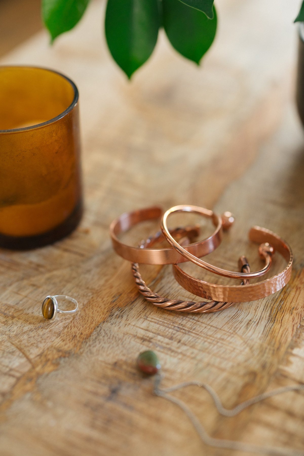 Pulsera de cobre Kopero, las cuatro versiones juntas sobre una mesa de madera con una vela y un anillo