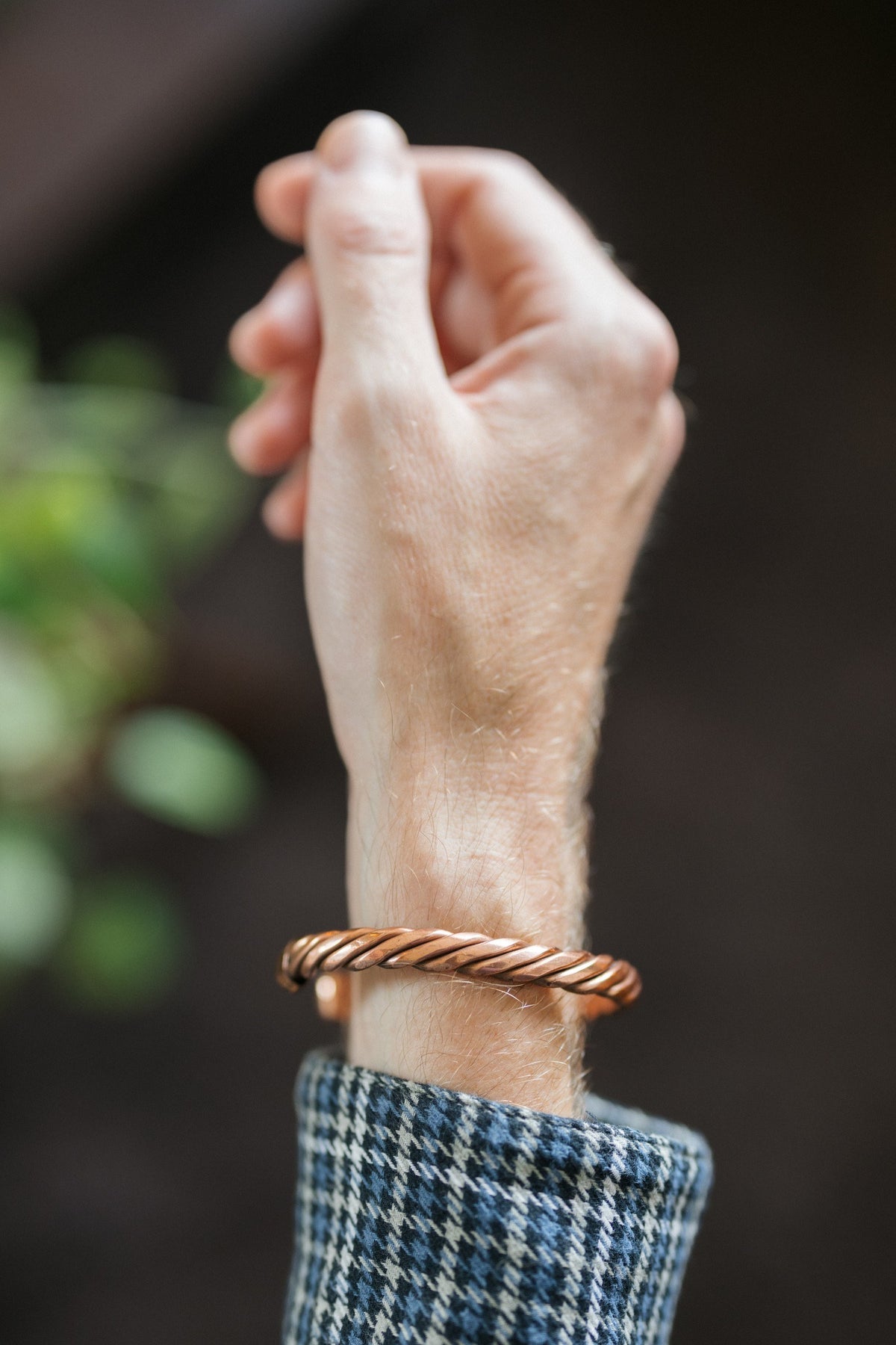 Pulsera de cobre Kopero Trenzado, en la muñeca, con la mano en alto sobre un fondo oscuro