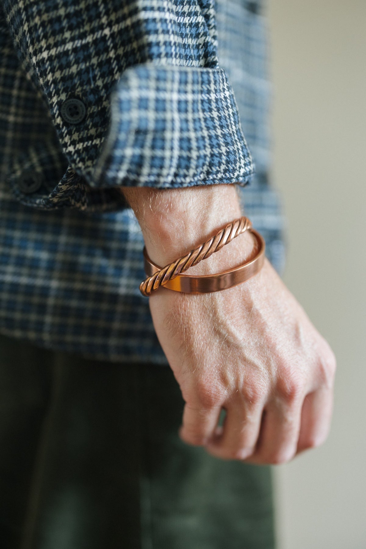 Pulsera de cobre Kopero Trenzado, en la muñeca sobre una manga de camisa de cuadros, junto con una pulsera lisa