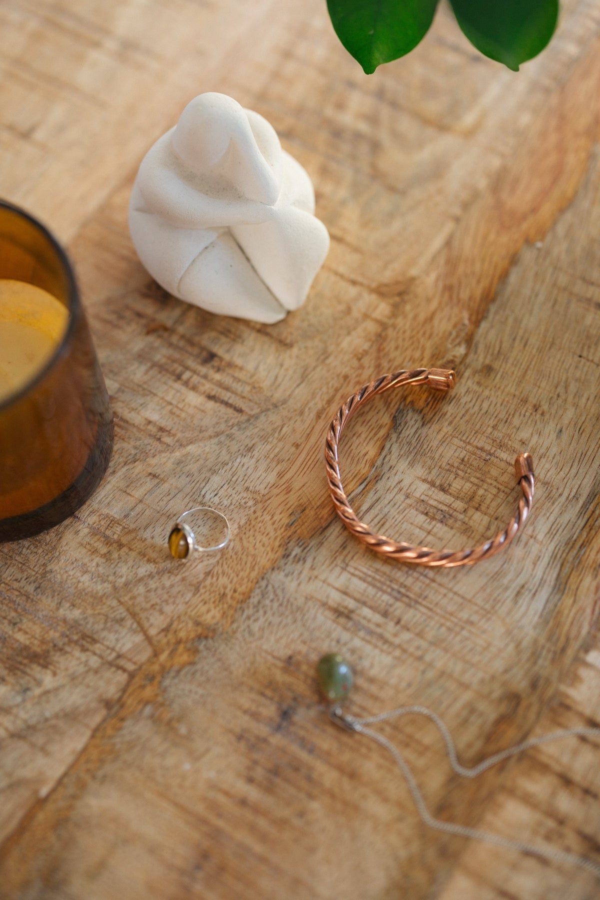 Pulsera de cobre Kopero Trenzado, sobre una mesa de madera junto a una figura y un anillo
