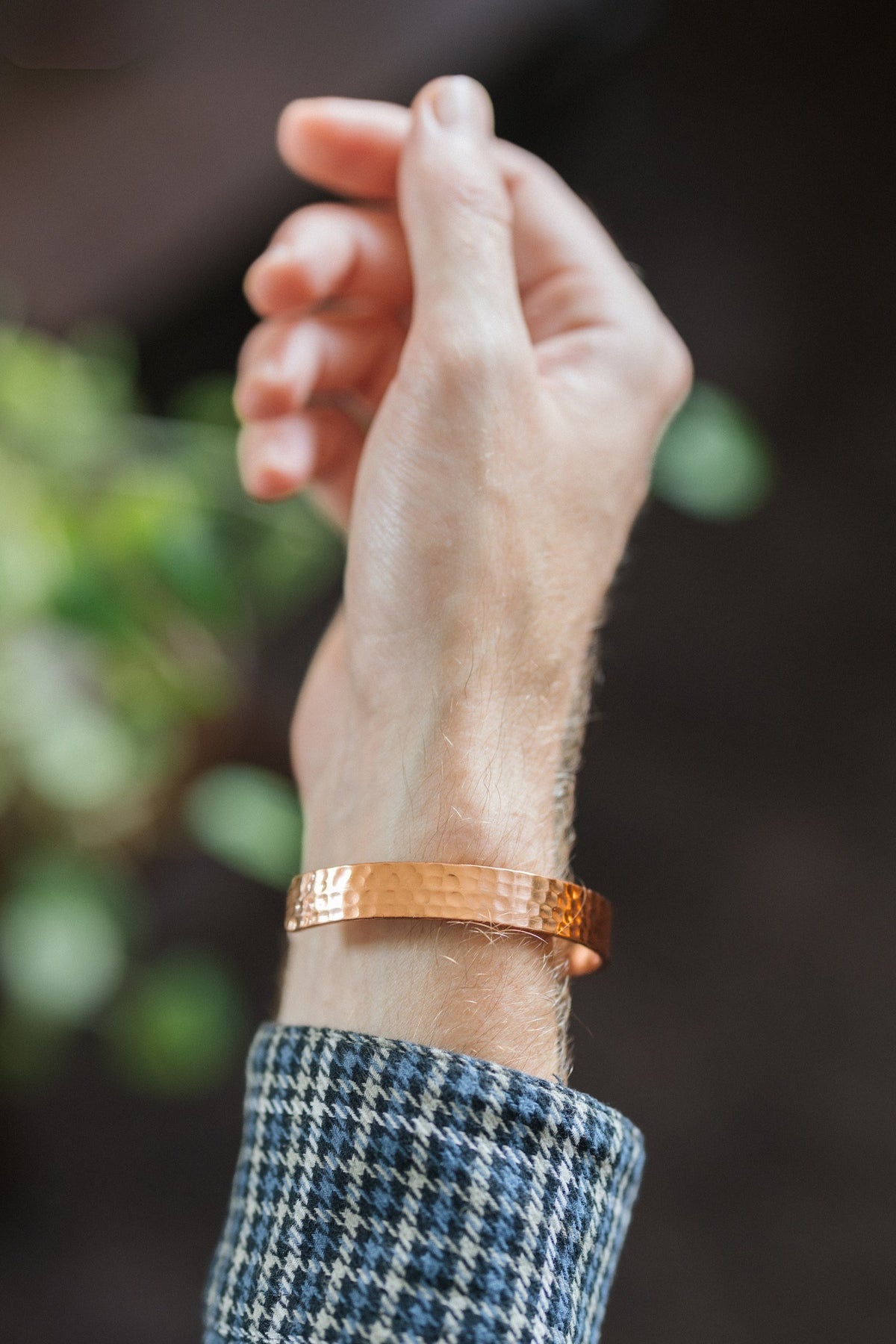 Pulsera de cobre Kopero Martillado, en la muñeca, con la mano en alto sobre un fondo oscuro