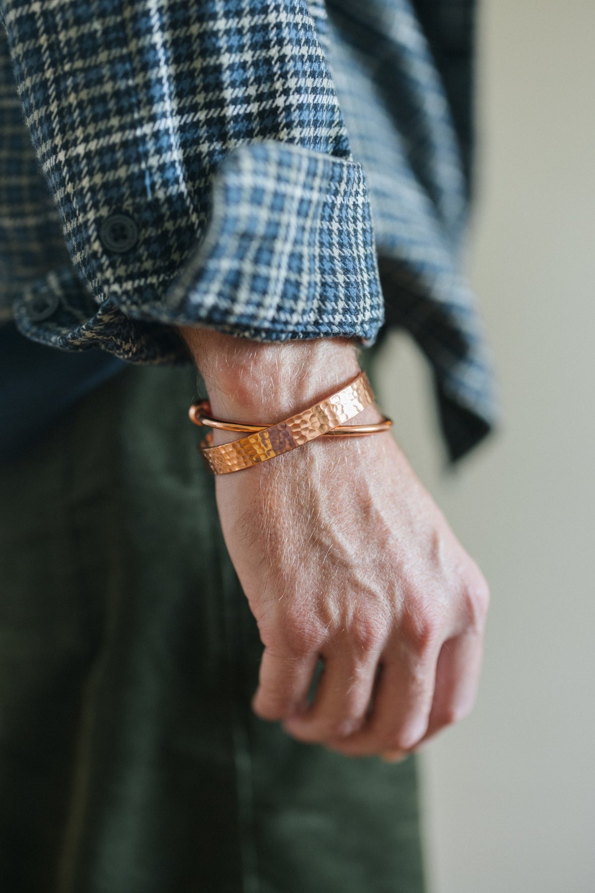 Pulsera de cobre Kopero Martillado, en la muñeca sobre una manga de camisa de cuadros, junto con una pulsera lisa