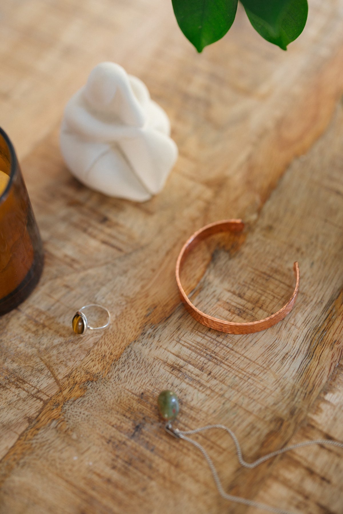 Pulsera de cobre Kopero Martillado, sobre una mesa de madera junto a una figura y un anillo