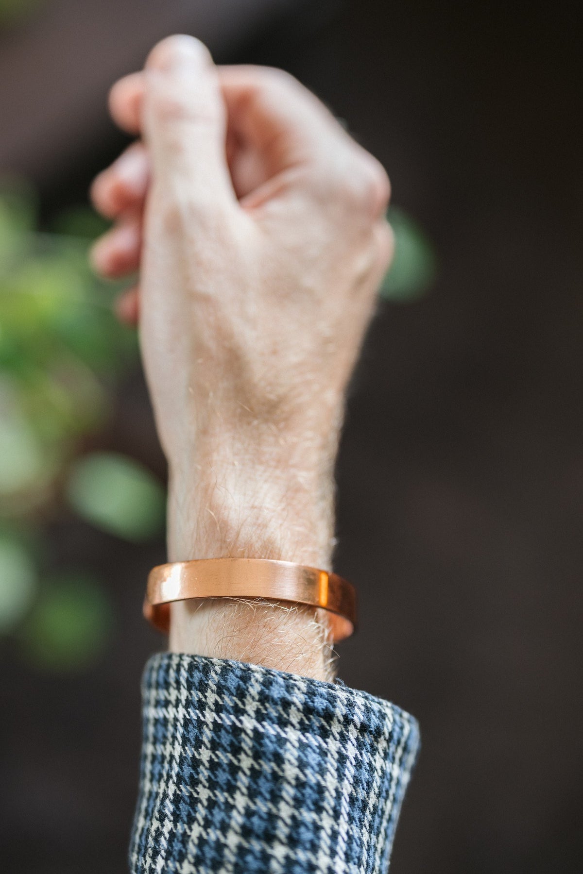 Pulsera de cobre Kopero Liso, en la muñeca, con la mano en alto sobre un fondo oscuro