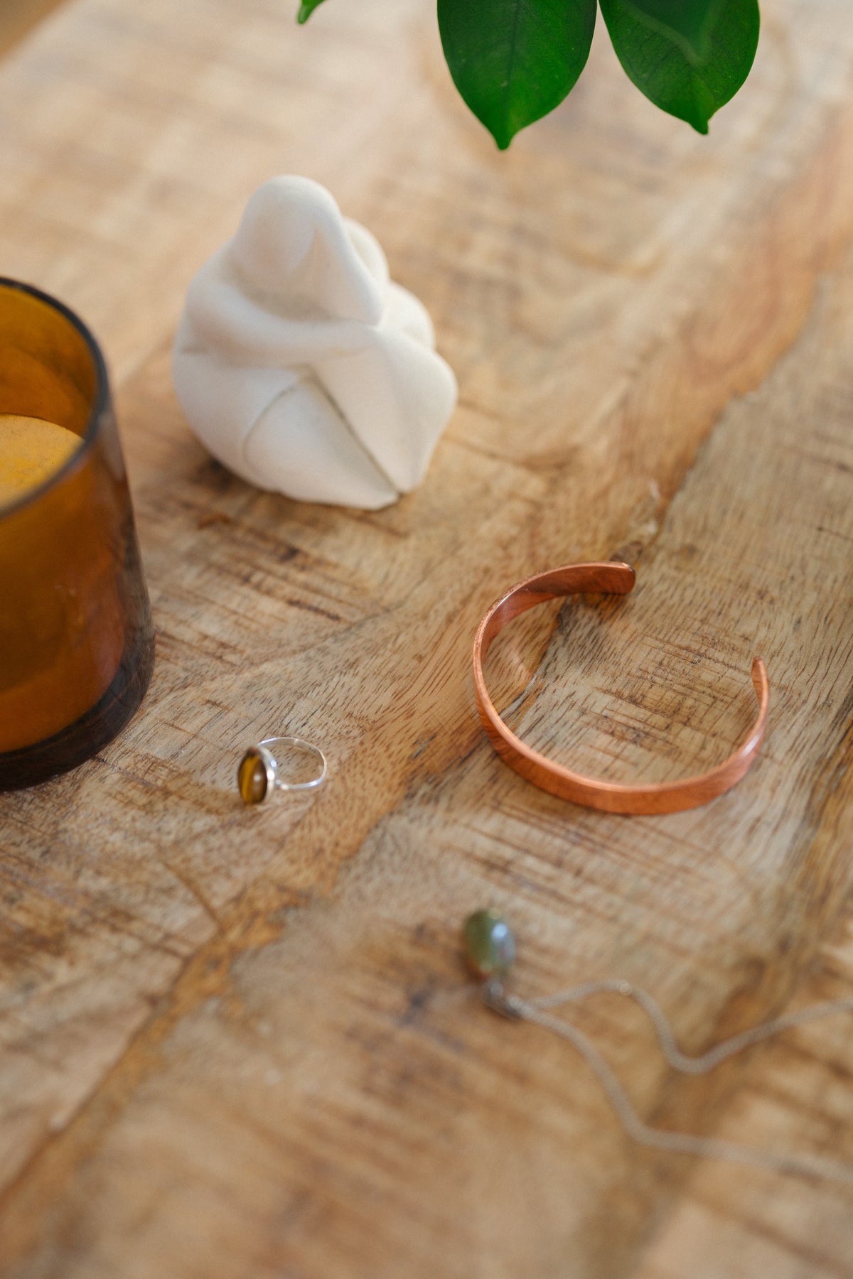 Pulsera de cobre Kopero Liso, sobre una mesa de madera junto a una figura y un anillo