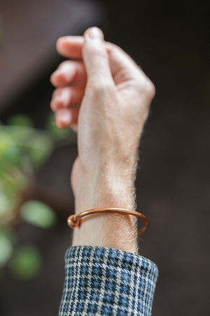 Pulsera de cobre Kopero Redondo, en la muñeca, con la mano en alto sobre un fondo oscuro