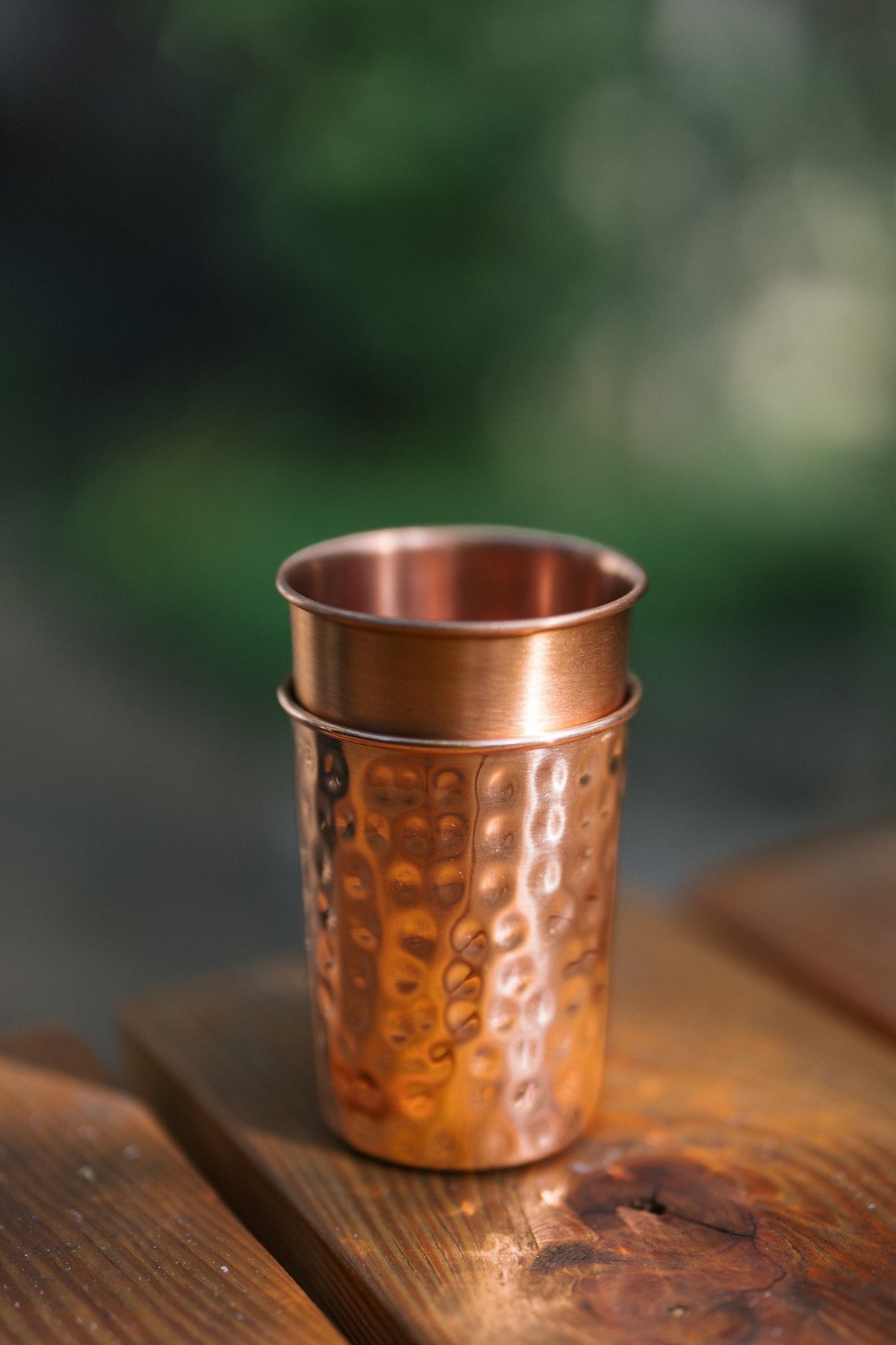 Vaso de cobre Kopero, un vaso liso y uno martillado apilados sobre una mesa de madera