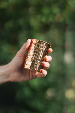 Vaso de cobre Kopero Martillado, en una mano sobre un fondo verde