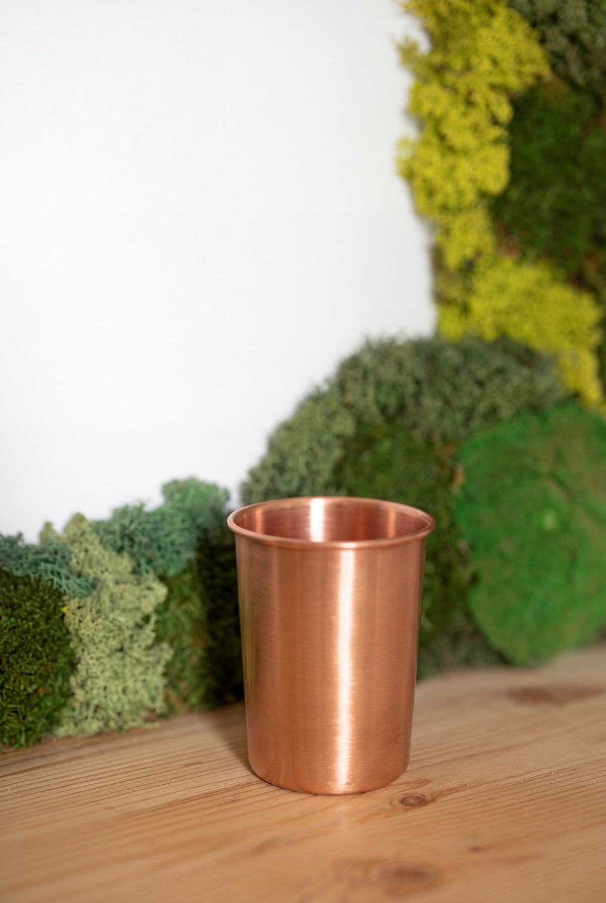 Vaso de Cobre Kopero Liso frente a un cuadro de musgo sobre una tabla de pino