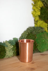 Vaso de Cobre Kopero Liso frente a un cuadro de musgo sobre una tabla de pino