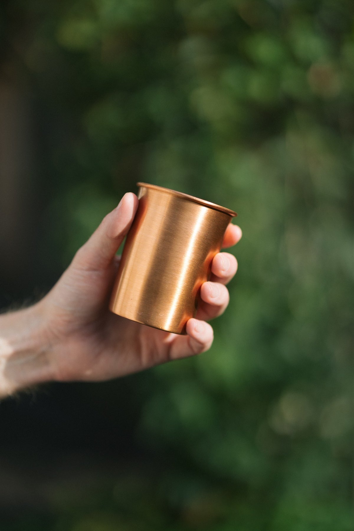 Vaso de cobre Kopero Liso, en una mano sobre un fondo verde