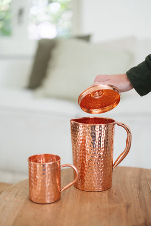 Jarra de cobre Kopero Martillado, mientras se levanta la tapa, con una taza al lado