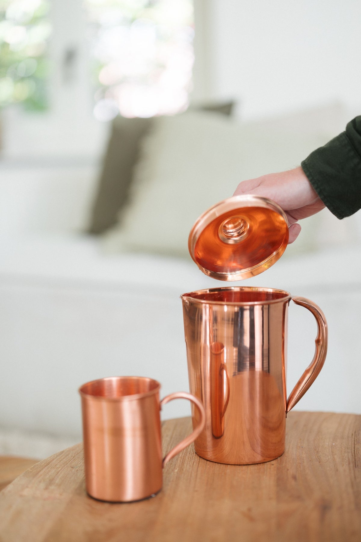 Jarra de cobre Kopero Liso, mientras se levanta la tapa, con una taza al lado