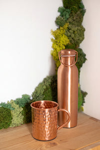 Taza de cobre Kopero Premium Martillada junto a una botella de cobre de la colección Kopero