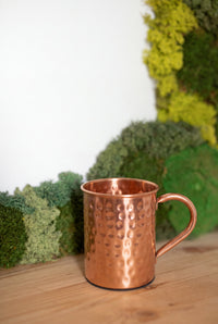 Taza de Cobre Kopero Martillada frente a un cuadro de musgo sobre una tabla de pino