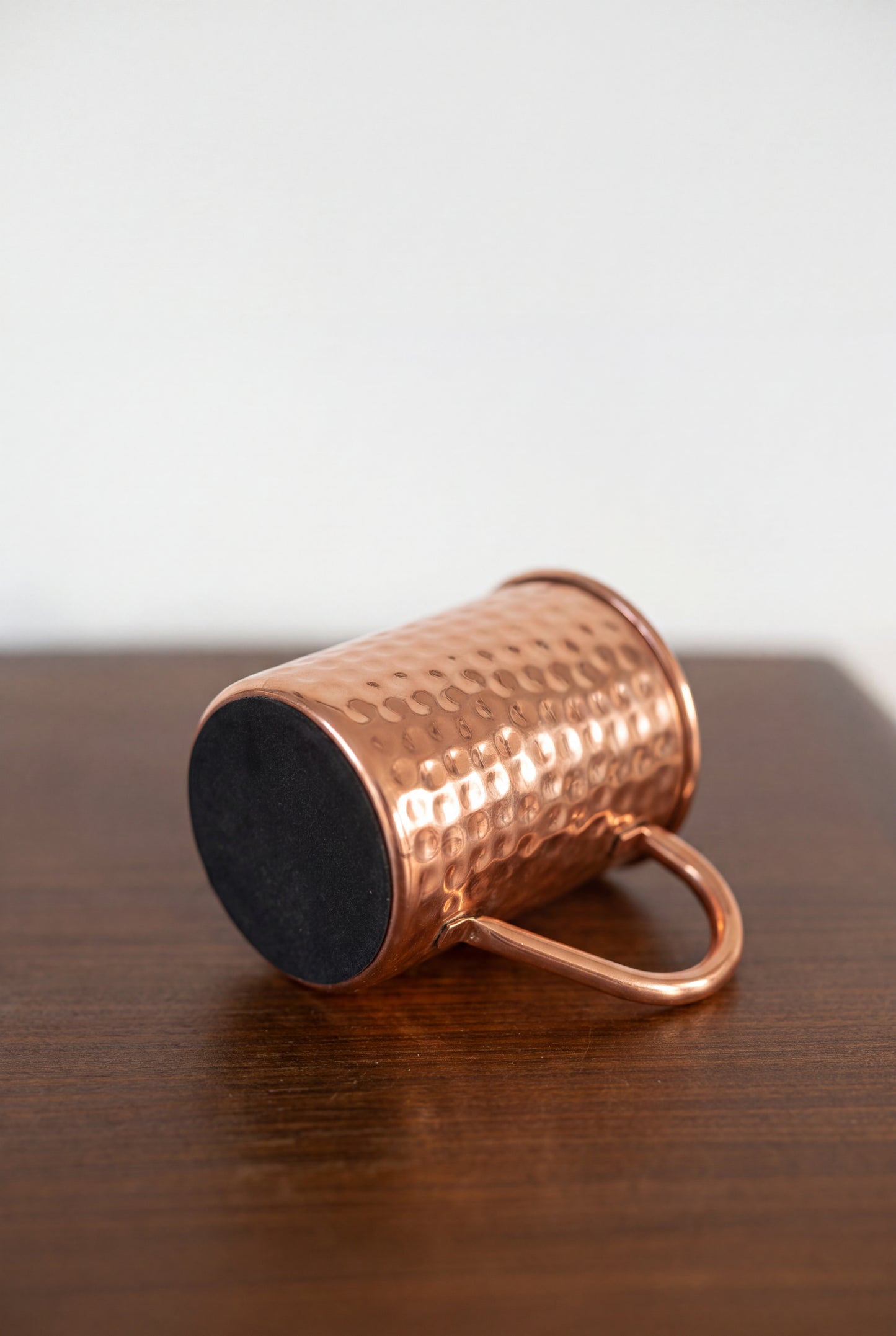 Taza de cobre Kopero Premium Martillada tumbada, con la base de fieltro visible