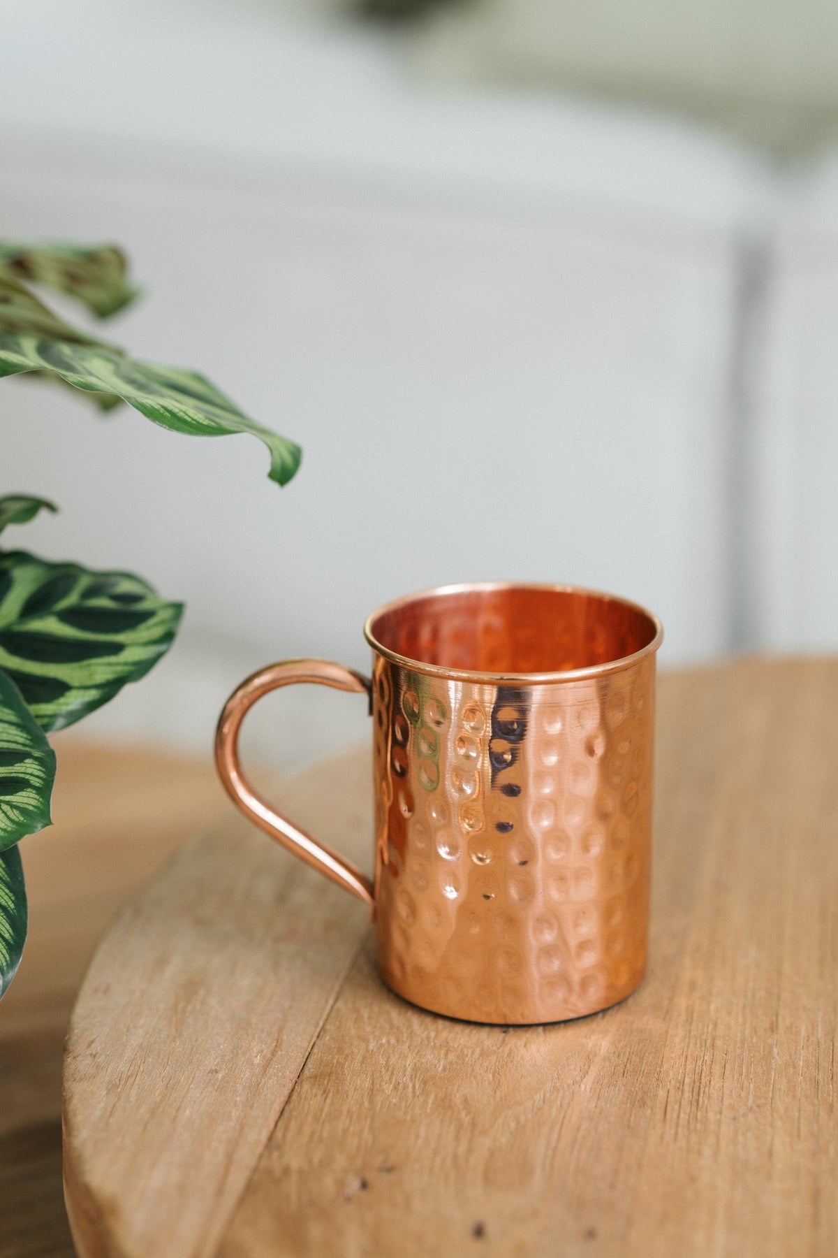 Taza de cobre Kopero Martillado, sobre una mesa redonda de madera frente a un sofá