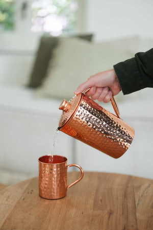 Taza de cobre Kopero Martillado, mientras se vierte agua desde una jarra de cobre