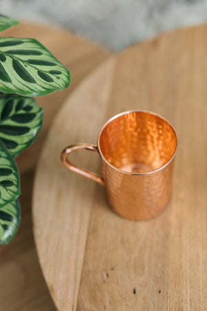 Taza de cobre Kopero Martillado, de lado sobre una mesa redonda de madera