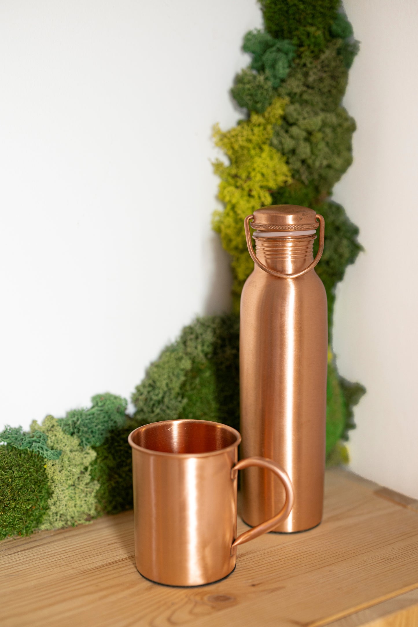 Taza de cobre Kopero Premium Lisa junto a una botella de cobre de la colección Kopero