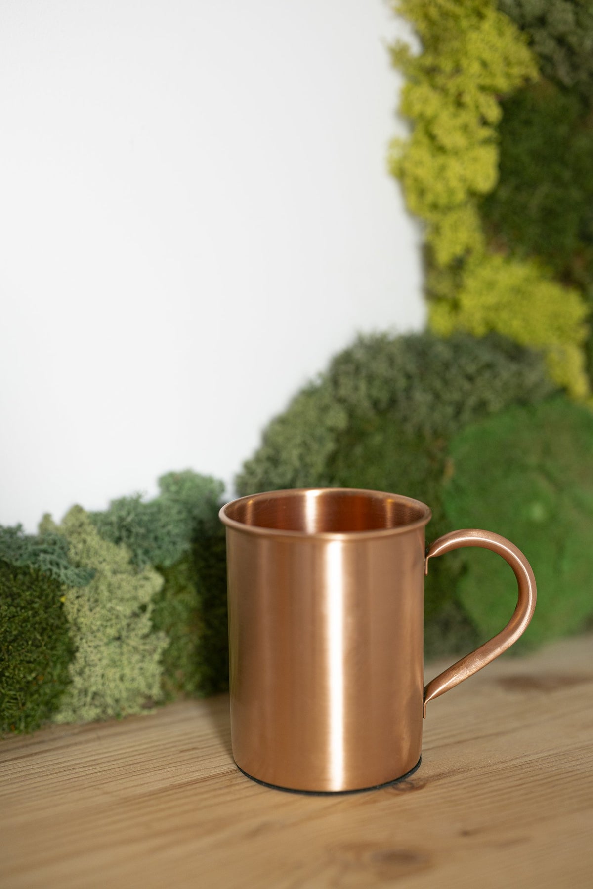 Taza de Cobre Kopero Lisa frente a un cuadro de musgo sobre una tabla de pino