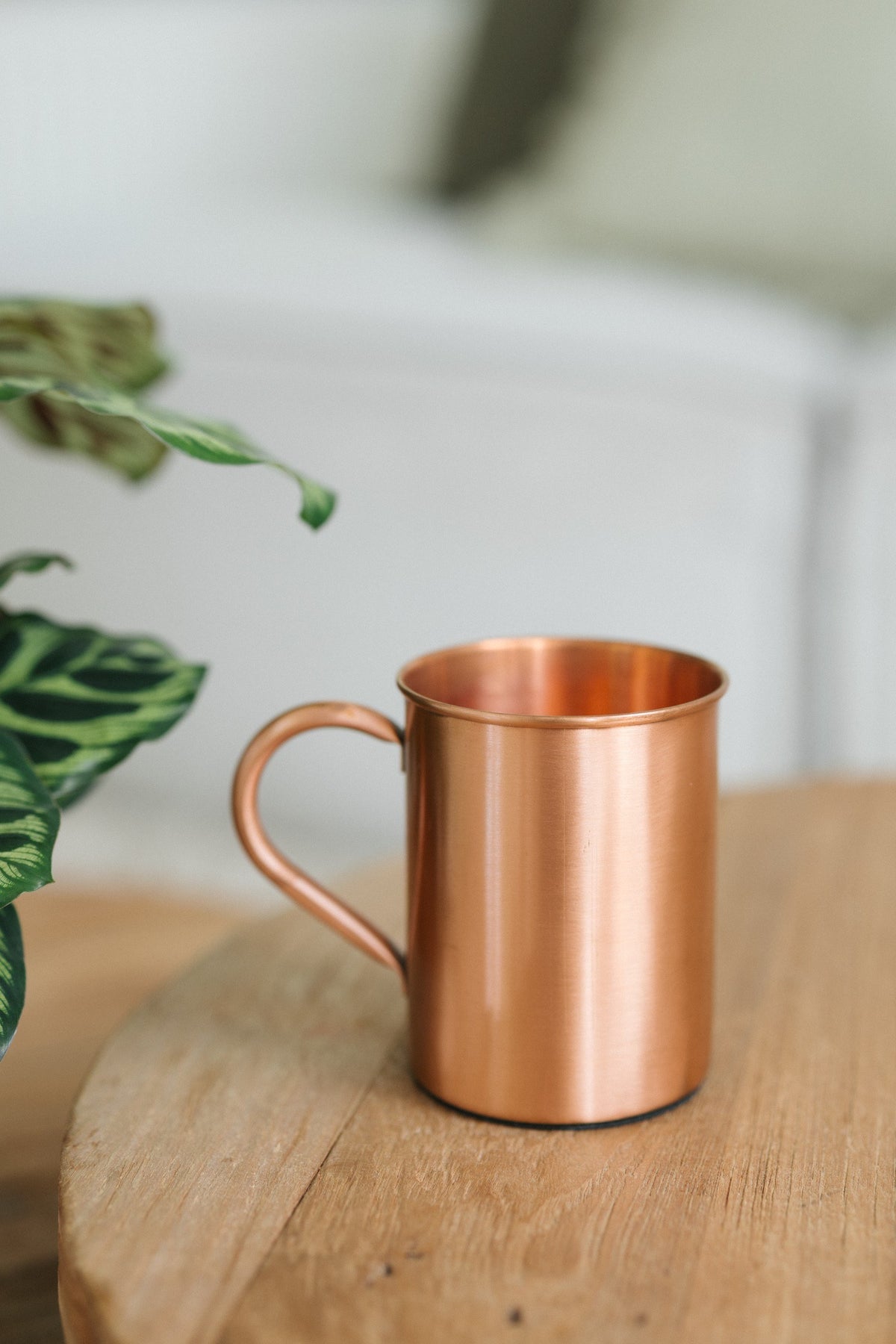 Taza de cobre Kopero Liso, sobre una mesa redonda de madera frente a un sofá