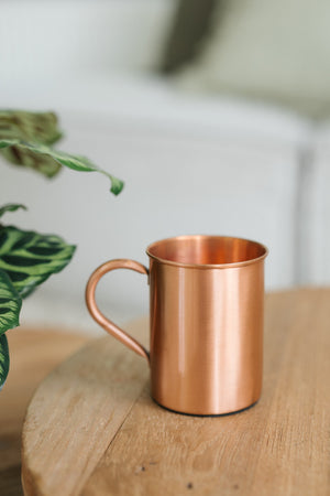 Taza de cobre Kopero Liso, sobre una mesa redonda de madera frente a un sofá