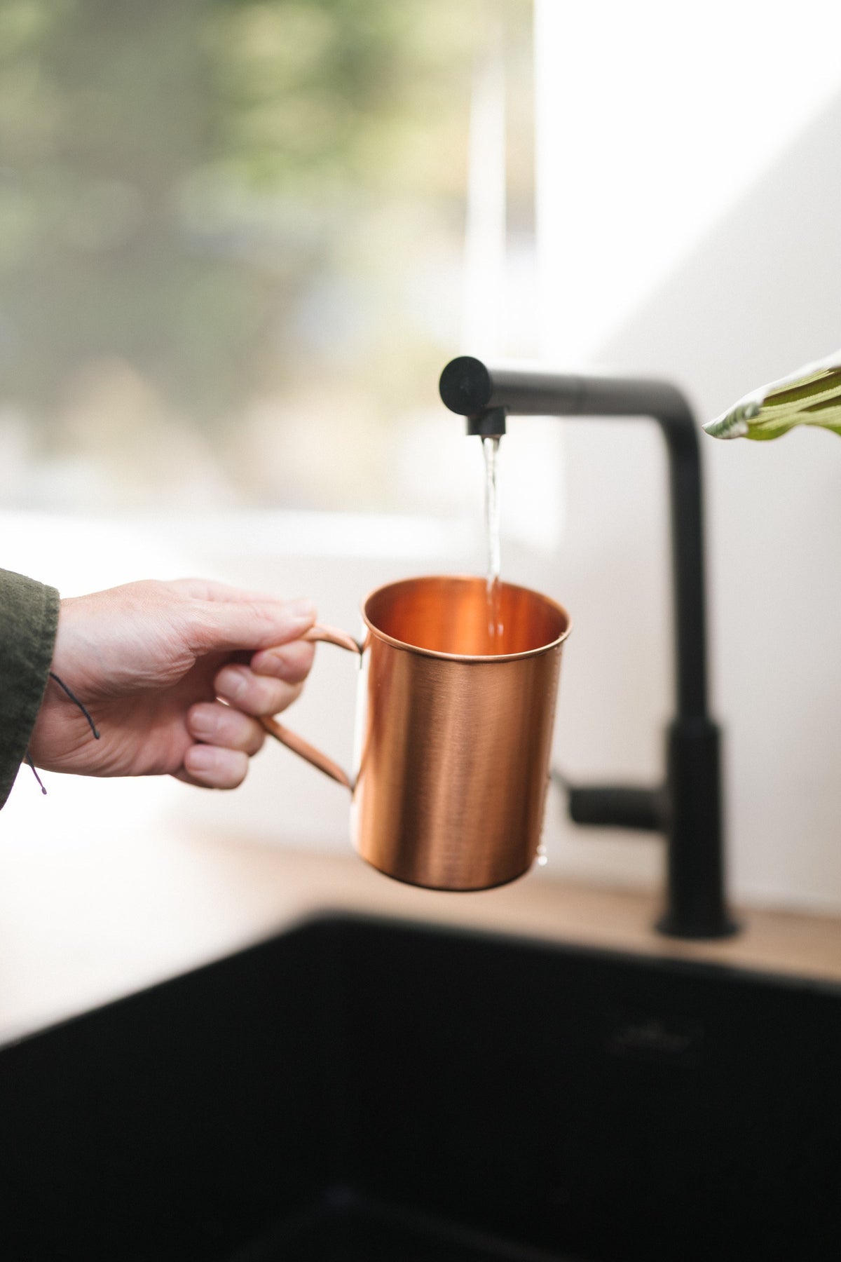 Taza de cobre Kopero Liso, en una mano bajo el grifo