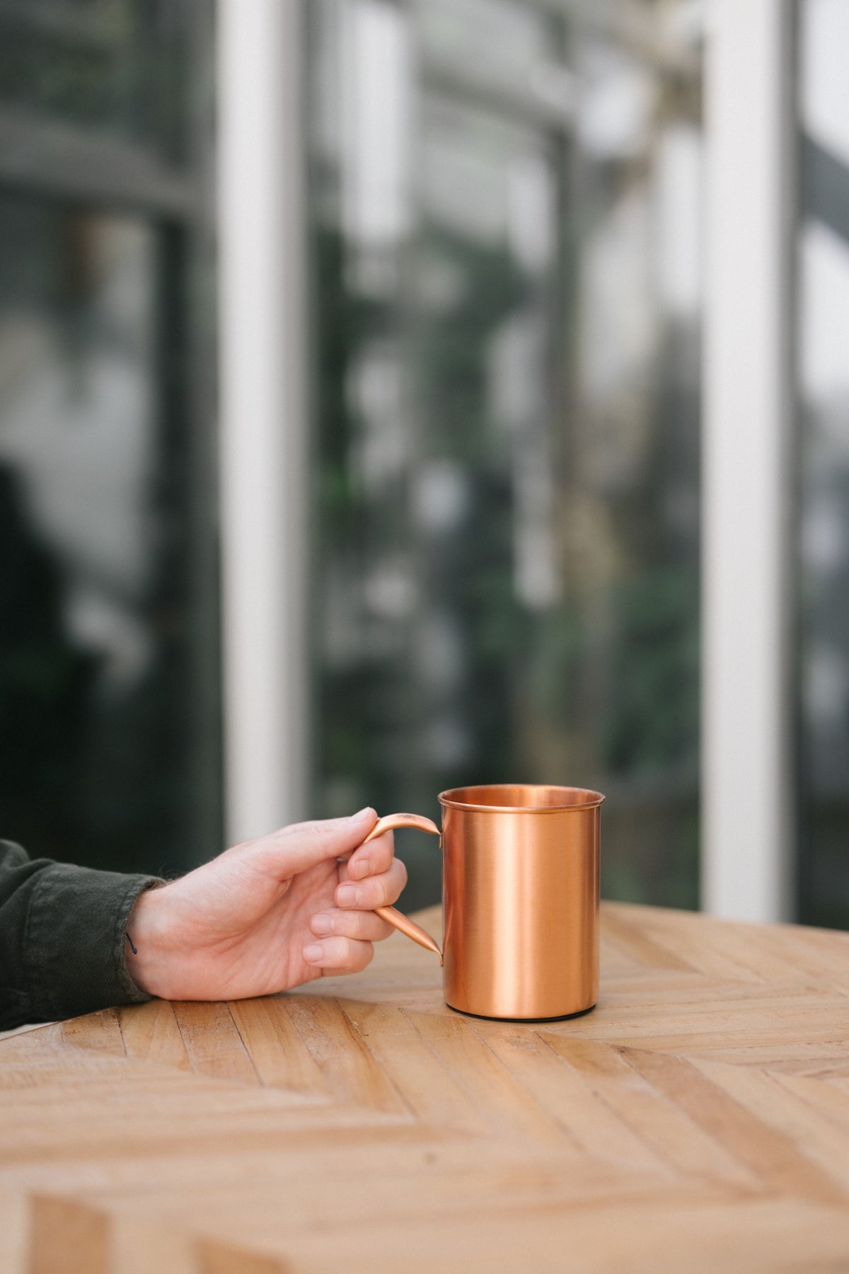 Taza de cobre Kopero Liso, sobre una mesa de madera, con una mano en el asa
