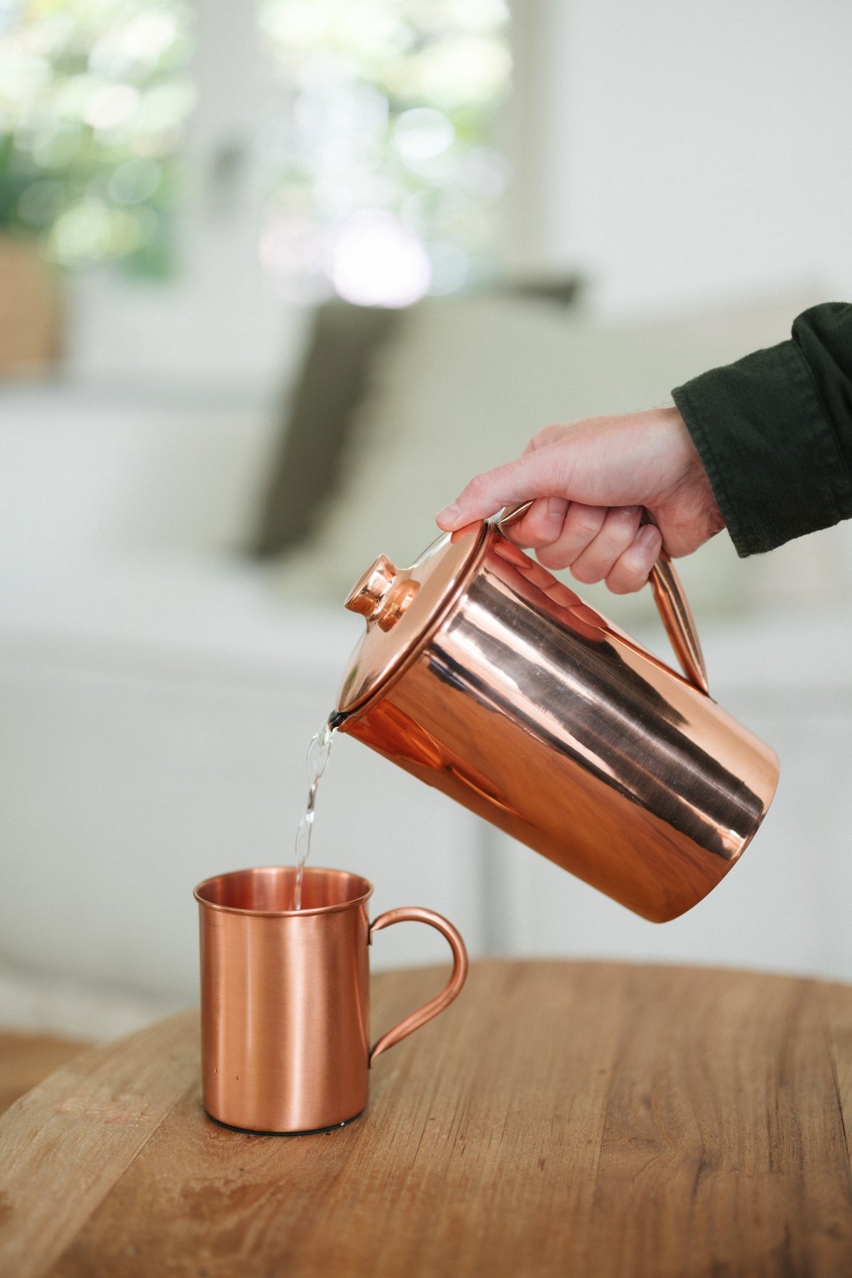 Taza de cobre Kopero Liso, mientras se vierte agua desde una jarra de cobre
