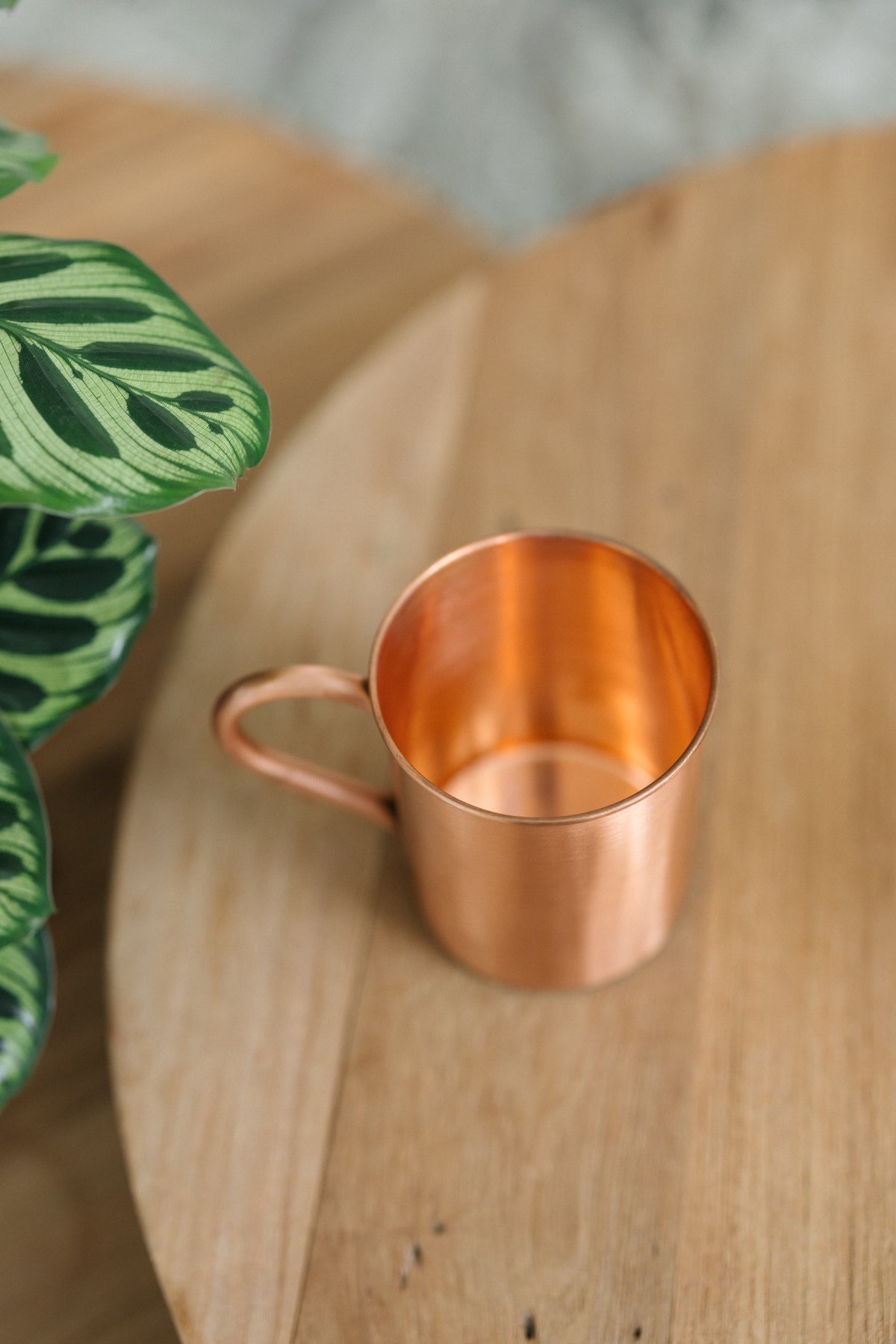 Taza de cobre Kopero Liso, de lado sobre una mesa redonda de madera