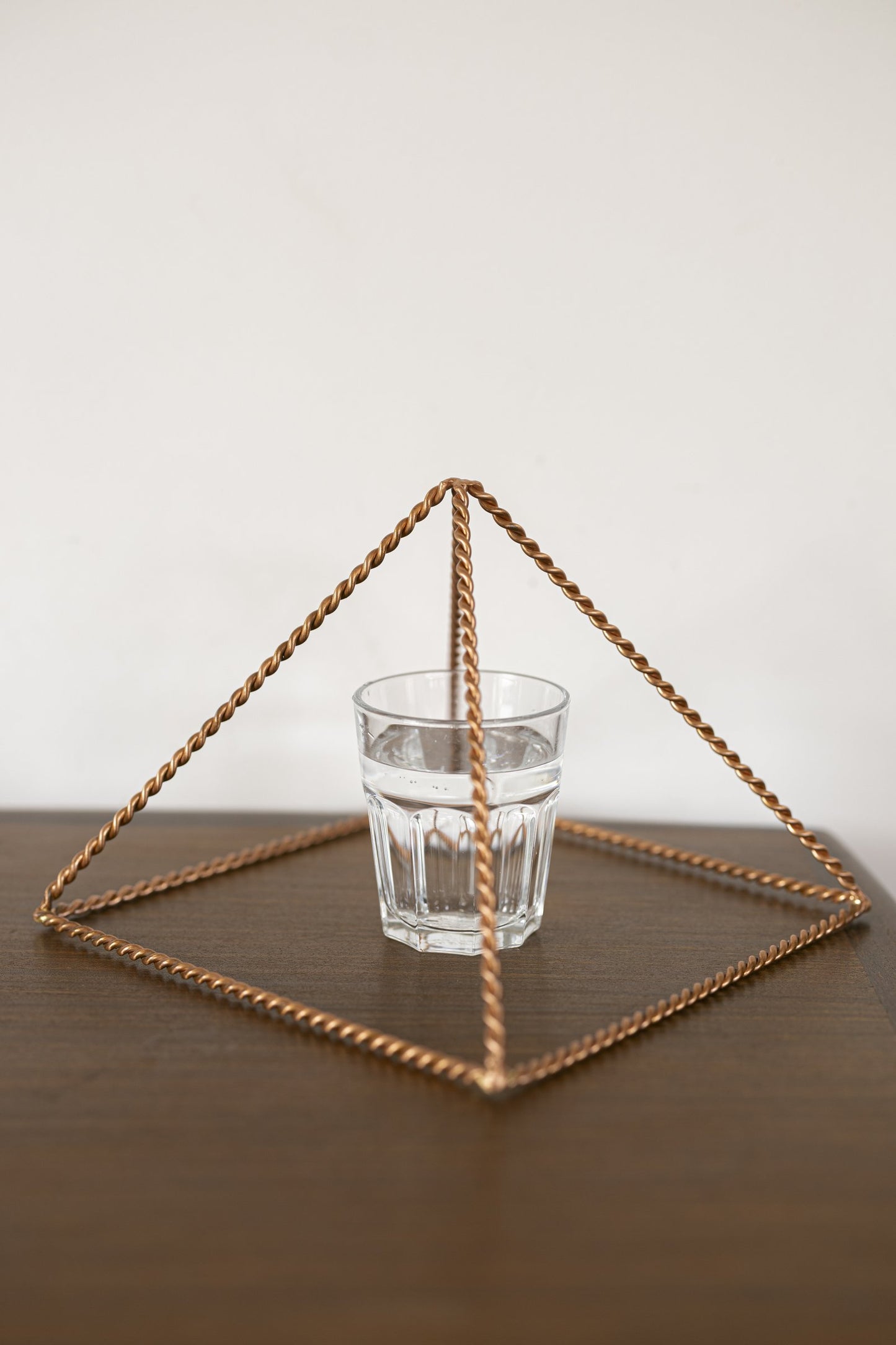 Pirámide Energizante de Cobre Kopero Trenzada Grande (23,56 cm) sobre un vaso de agua