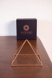 Pirámide Energizante de Cobre Kopero Trenzada Pequeña (14,56 cm) frente a la caja de regalo negra Kopero