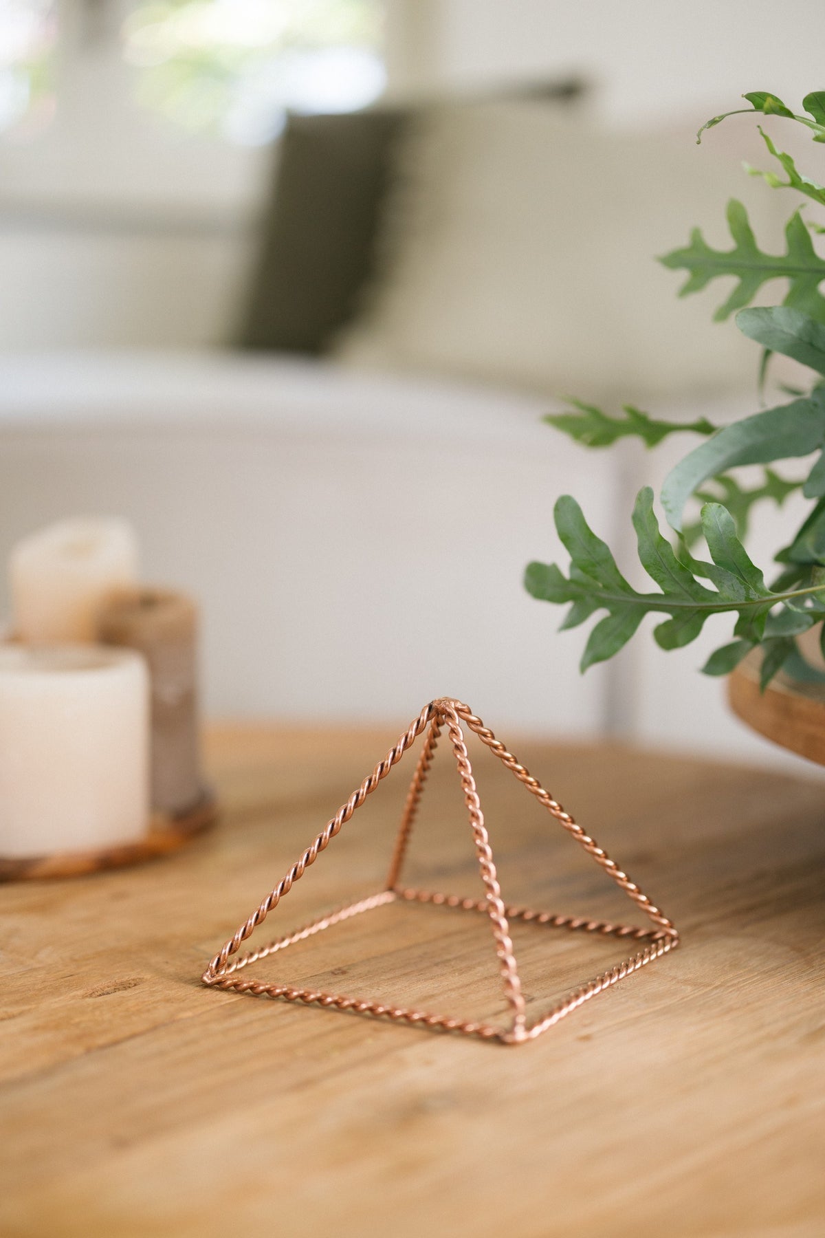 Pirámide energizante de cobre trenzada Kopero Pequeña (14,56 cm), sobre una mesa de madera junto a unas velas