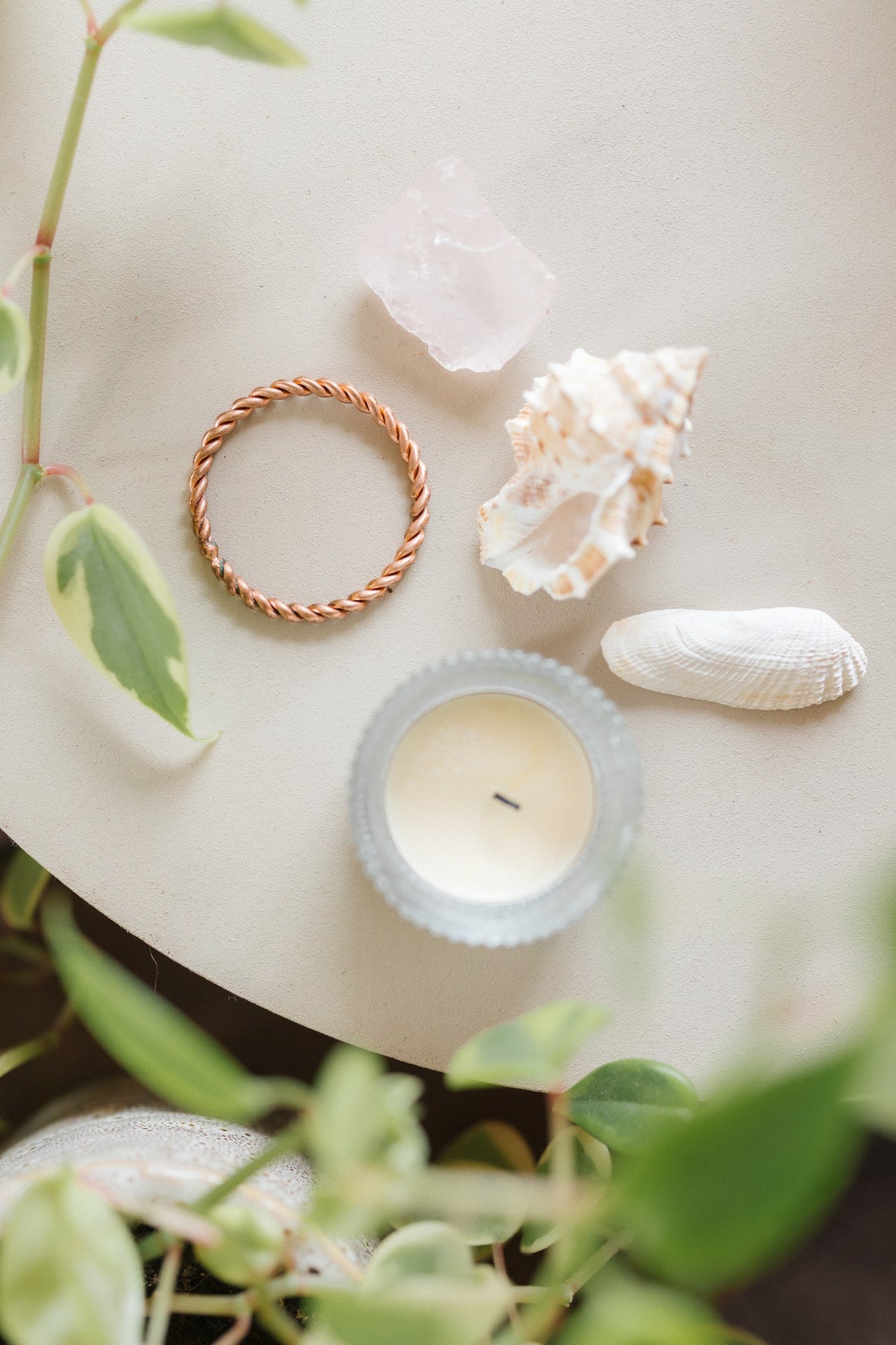Anillo tensor de cobre Kopero, sobre una mesita color crema junto a un cuarzo rosa, una concha y una vela de té