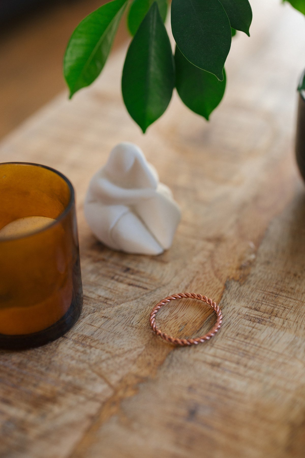 Anillo tensor de cobre Kopero, sobre una mesa de madera junto a un portavelas de cristal y una figura