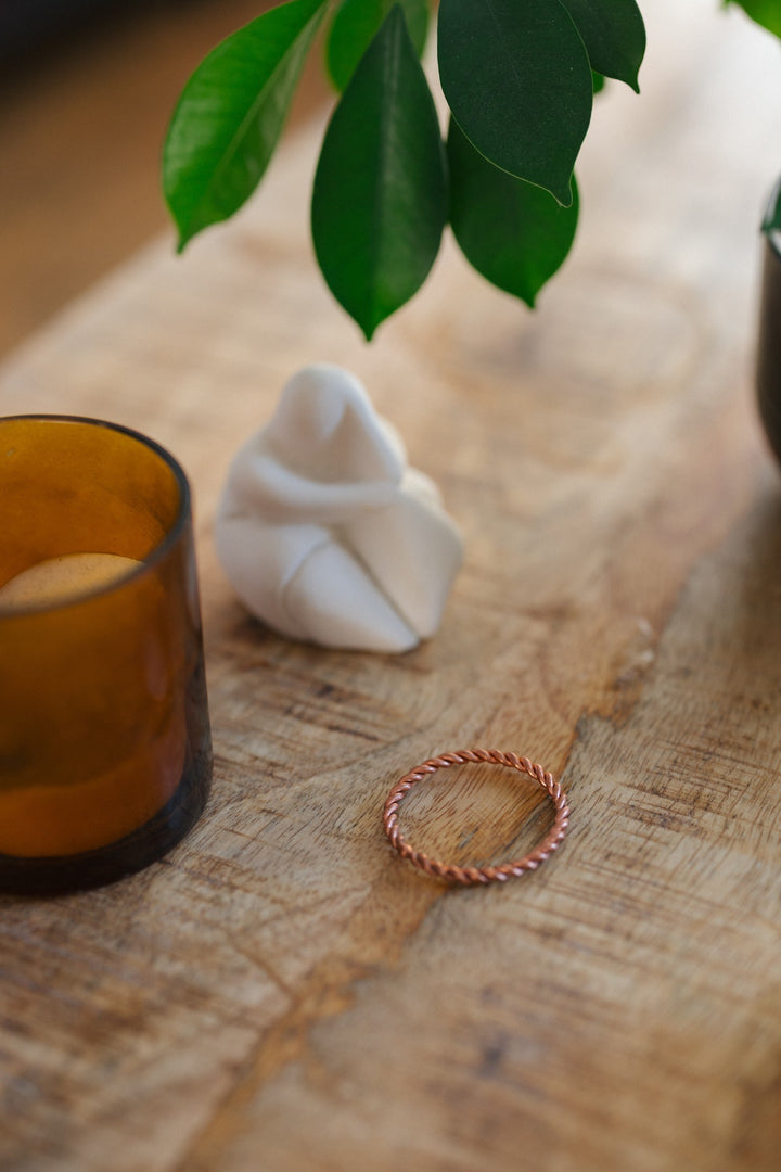 Anillo tensor de cobre Kopero, sobre una mesa de madera junto a un portavelas de cristal y una figura
