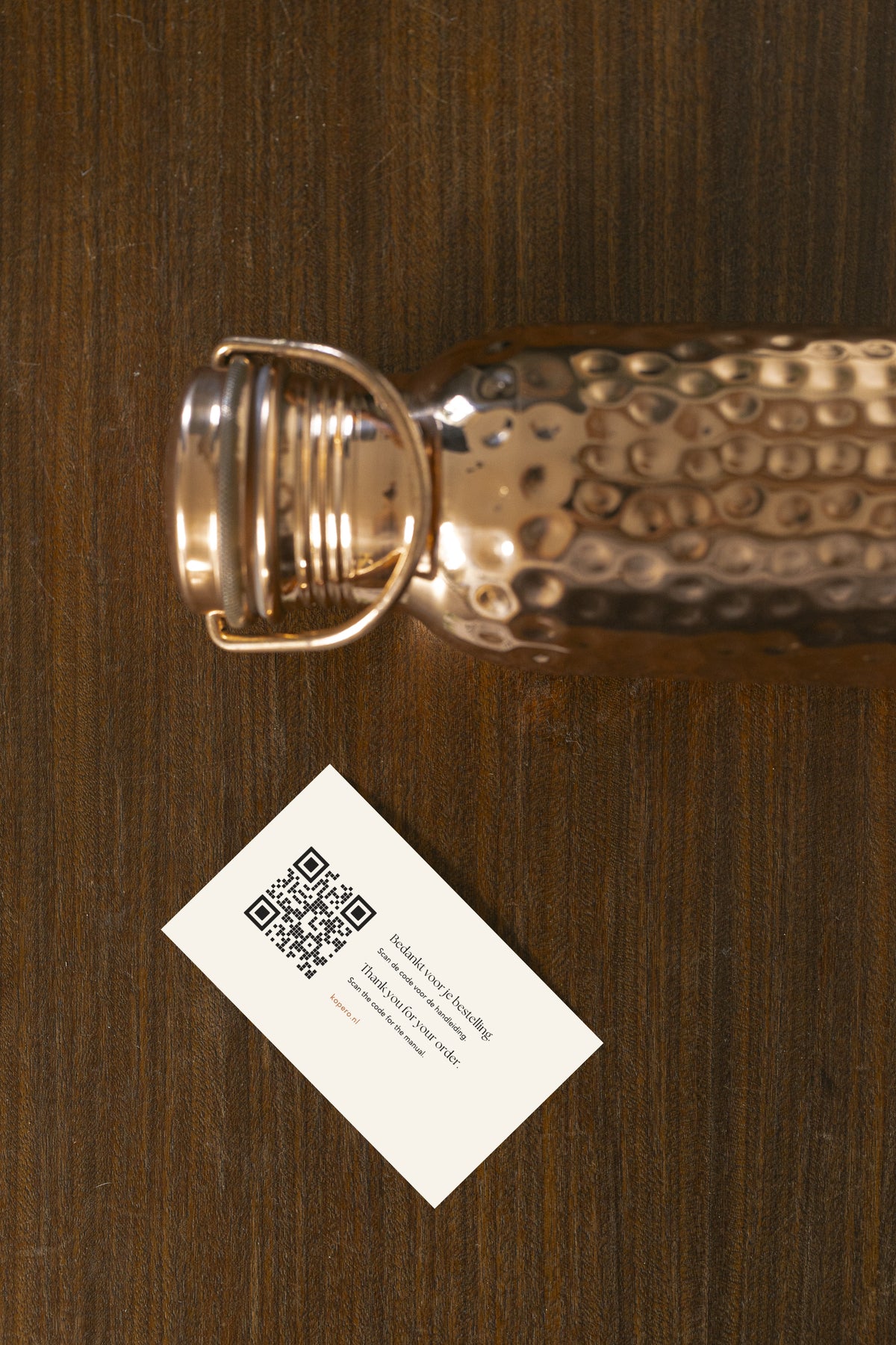 Botella de agua de cobre Kopero Martillada vista desde arriba con tarjeta de agradecimiento y código QR para el manual