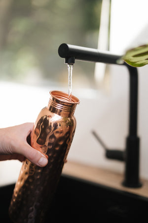 Botella de agua de cobre Kopero Martillado, bajo el grifo, mientras entra el agua