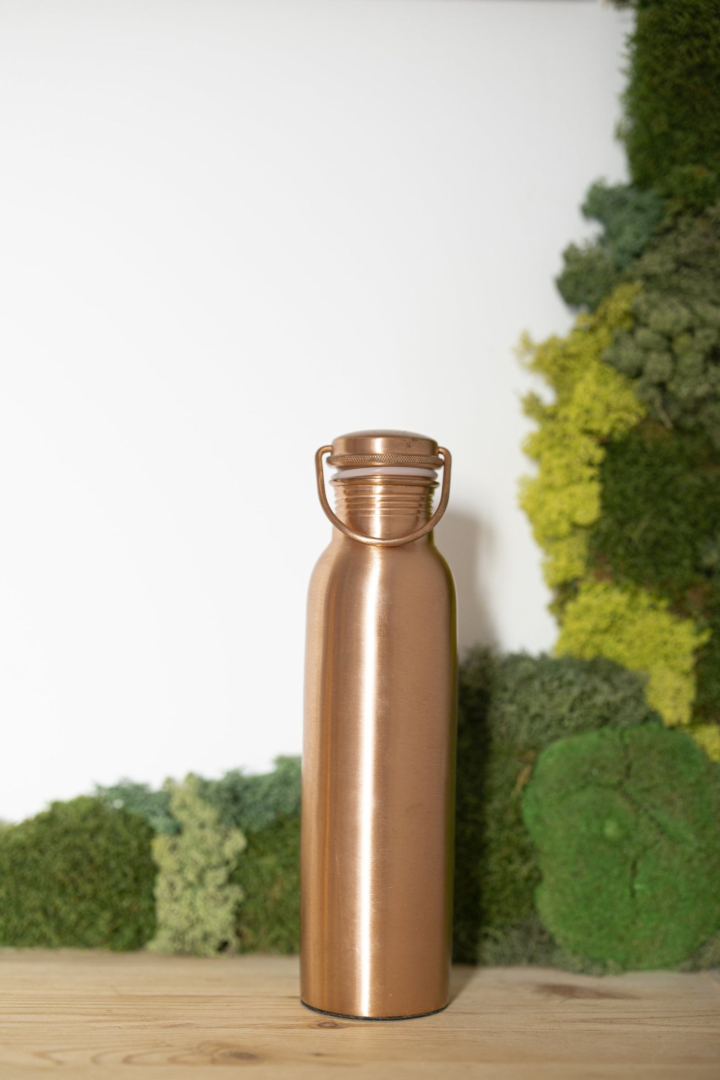 Botella de Agua de Cobre Kopero Lisa de 900 ml frente a un cuadro de musgo