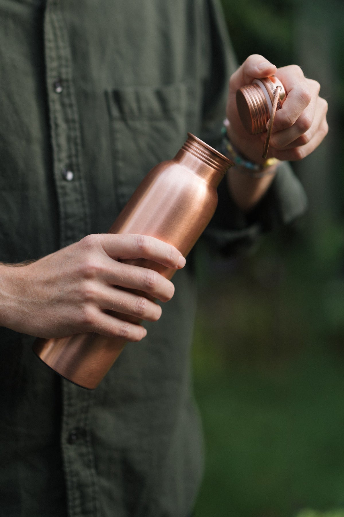 Botella de agua de cobre Kopero Liso, en una mano, mientras se desenrosca el tapón